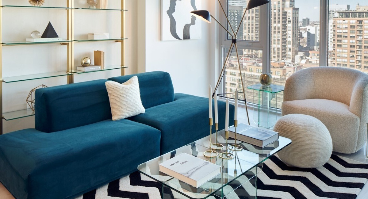 Cozy living room with teal sofa, chevron rug, glass coffee table, and floor-to-ceiling windows showcasing city views at 369 Grand apartments in Chicago