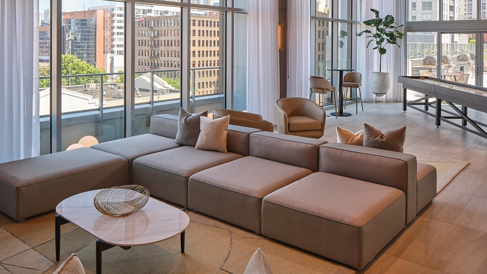 Resident lounge with modular sectional, lounge chairs, shuffleboard table, and floor-to-ceiling windows at 369 Grand apartments in Chicago