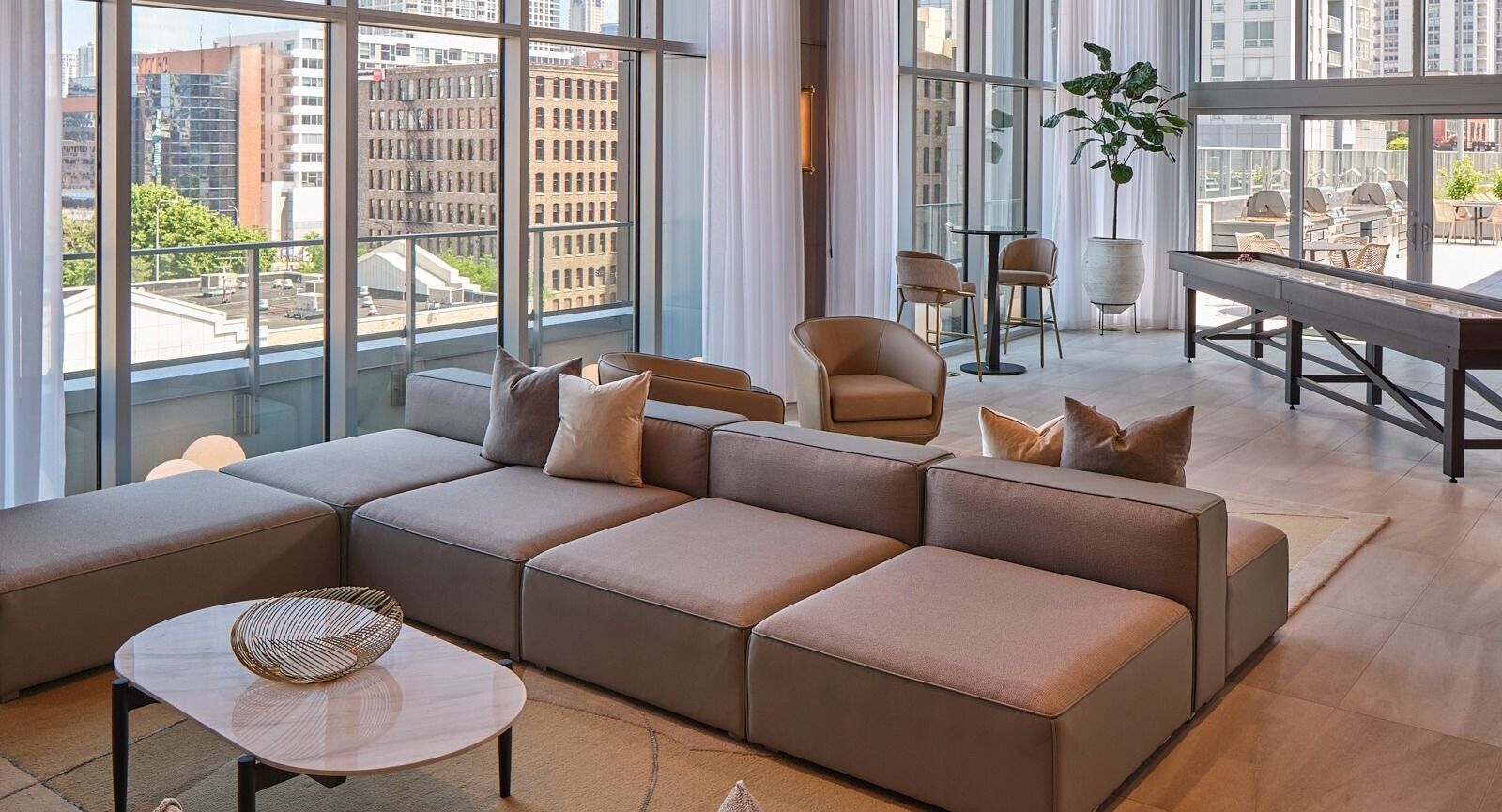 Resident lounge with modular sectional, lounge chairs, shuffleboard table, and floor-to-ceiling windows at 369 Grand apartments in Chicago
