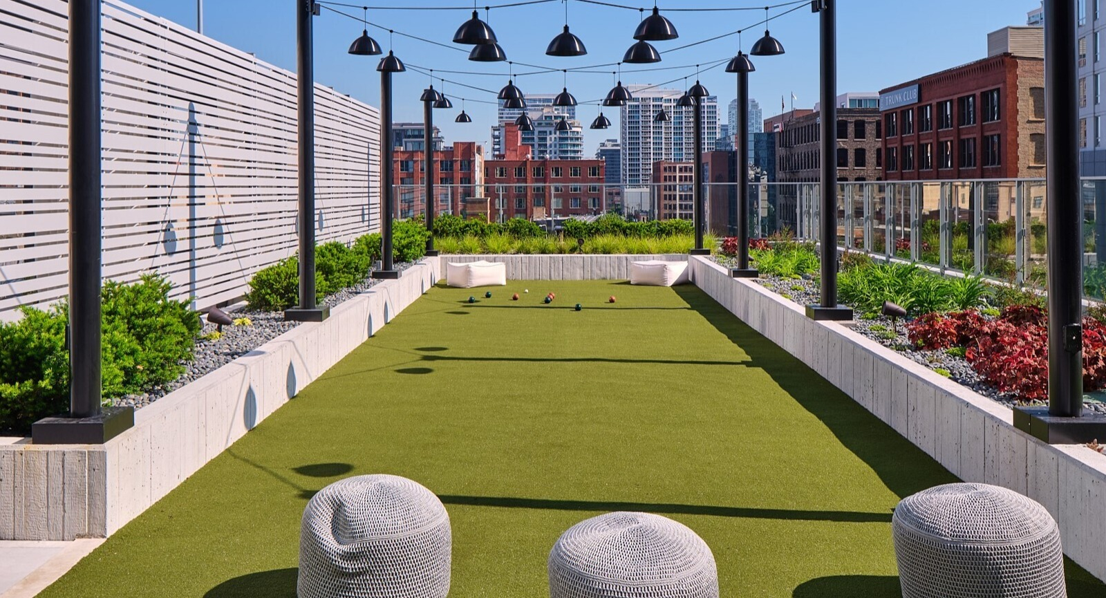 Outdoor bocce ball court with string lights, landscaped planters, and expansive skyline views on the rooftop at 369 Grand apartments in Chicago