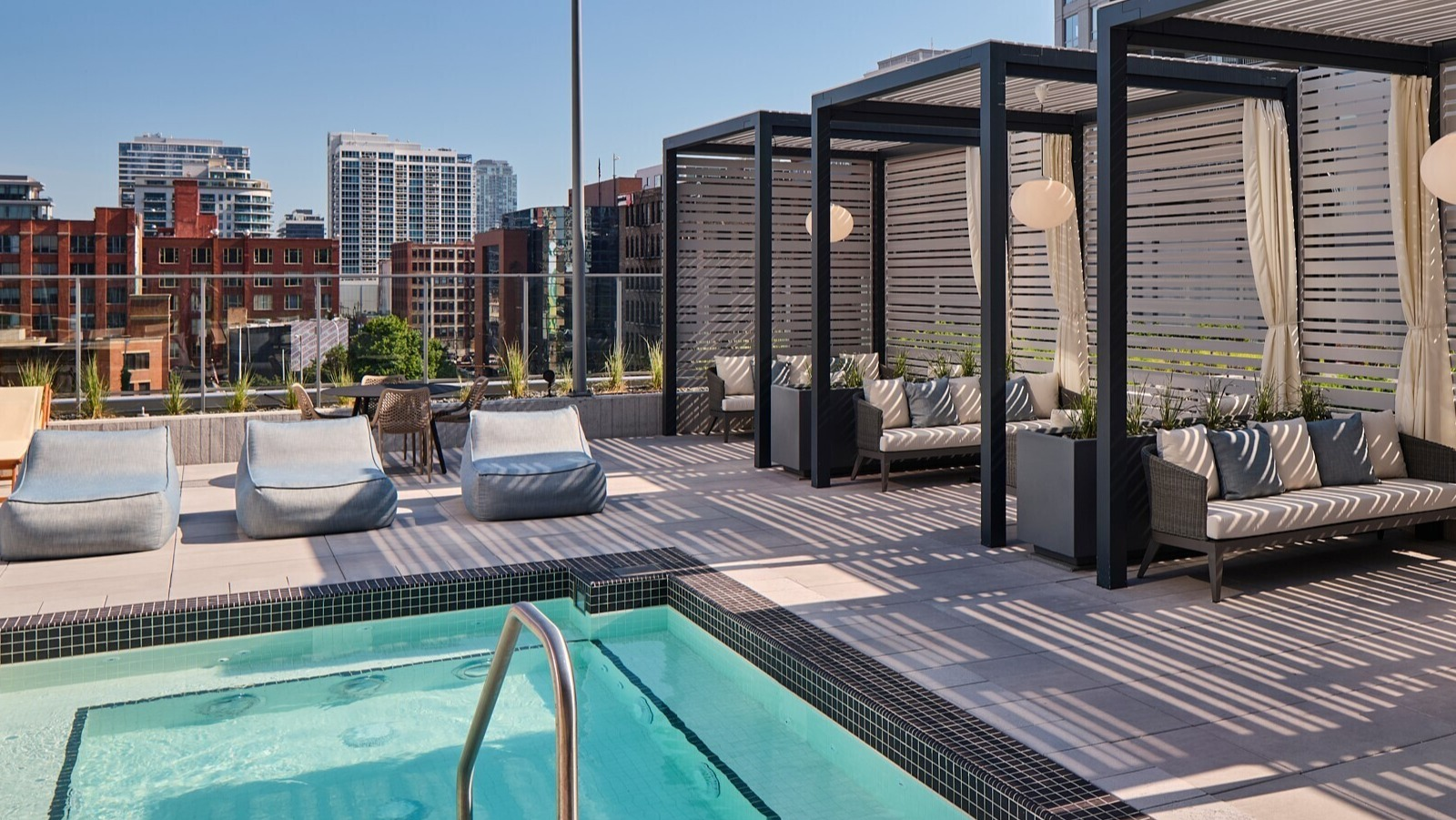 Private rooftop cabanas with cushioned seating beside a shallow spa pool, privacy screens, and skyline views at 369 Grand apartments in Chicago