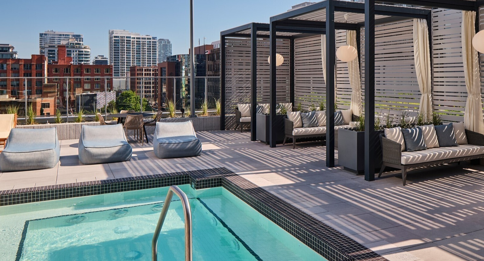 Private rooftop cabanas with cushioned seating beside a shallow spa pool, privacy screens, and skyline views at 369 Grand apartments in Chicago