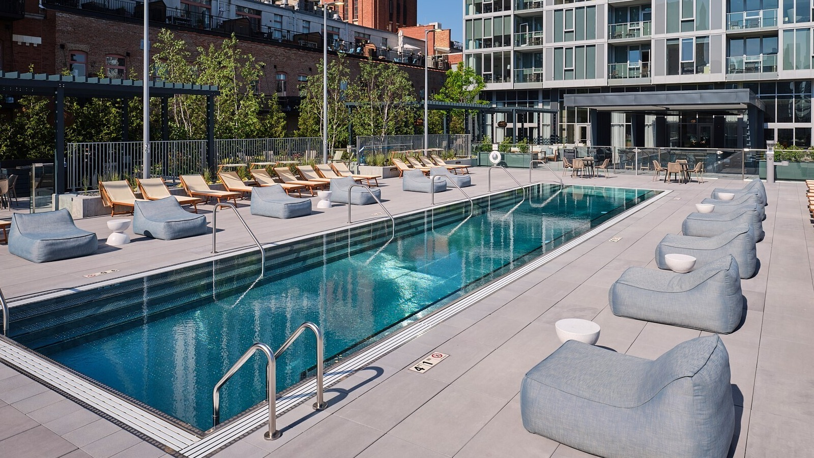 Rooftop lap pool with rows of loungers, cushioned daybeds, and a city skyline backdrop at 369 Grand apartments in Chicago