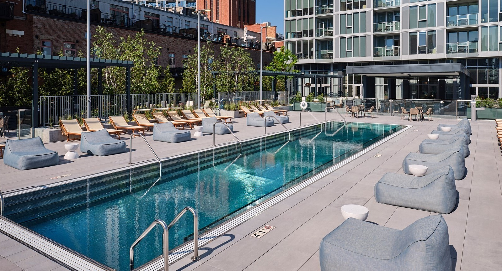 Rooftop lap pool with rows of loungers, cushioned daybeds, and a city skyline backdrop at 369 Grand apartments in Chicago