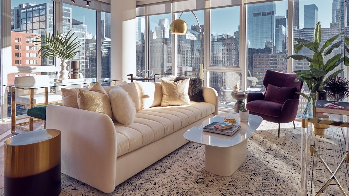 Sunlit living room with cream sofa, burgundy lounge chair, glass console, and floor-to-ceiling windows at 369 Grand apartments in Chicago