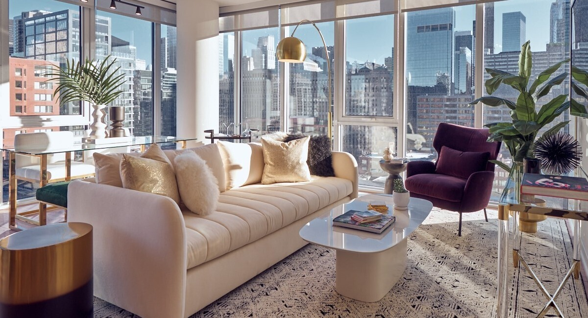 Sunlit living room with cream sofa, burgundy lounge chair, glass console, and floor-to-ceiling windows at 369 Grand apartments in Chicago