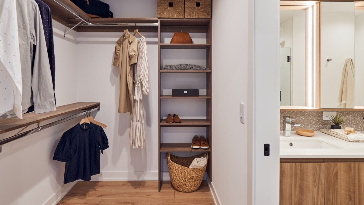 Spacious walk-in closet with custom wood shelving and hanging space leading to a sleek double-sink vanity at 369 Grand apartments in Chicago
