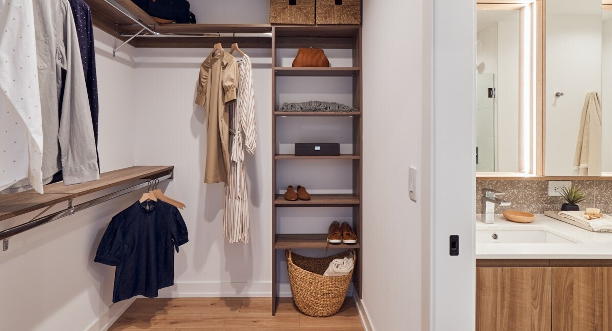 Spacious walk-in closet with custom wood shelving and hanging space leading to a sleek double-sink vanity at 369 Grand apartments in Chicago