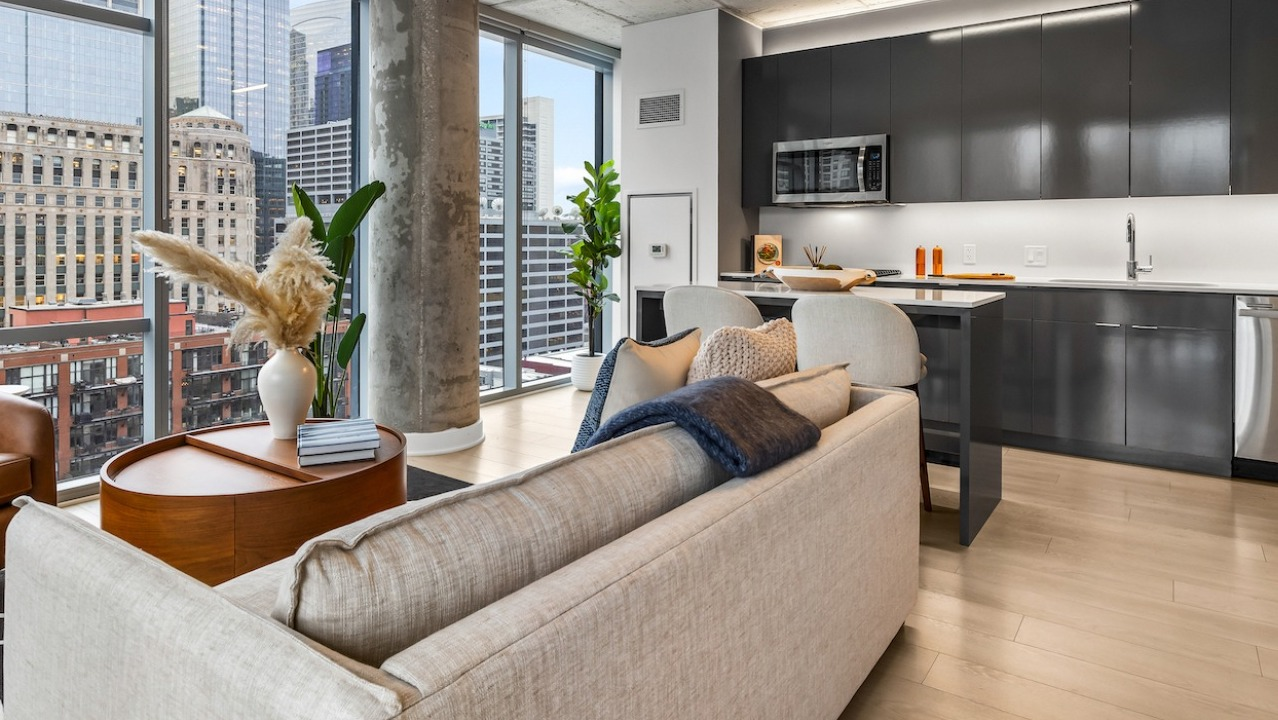 Corner living room at 3Eleven Luxury Apartments in Chicago with contemporary sofa, tall windows, and a sleek adjacent kitchen overlooking the skyline