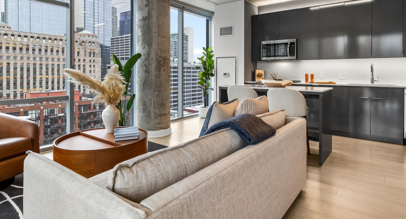 Corner living room at 3Eleven Luxury Apartments in Chicago with contemporary sofa, tall windows, and a sleek adjacent kitchen overlooking the skyline