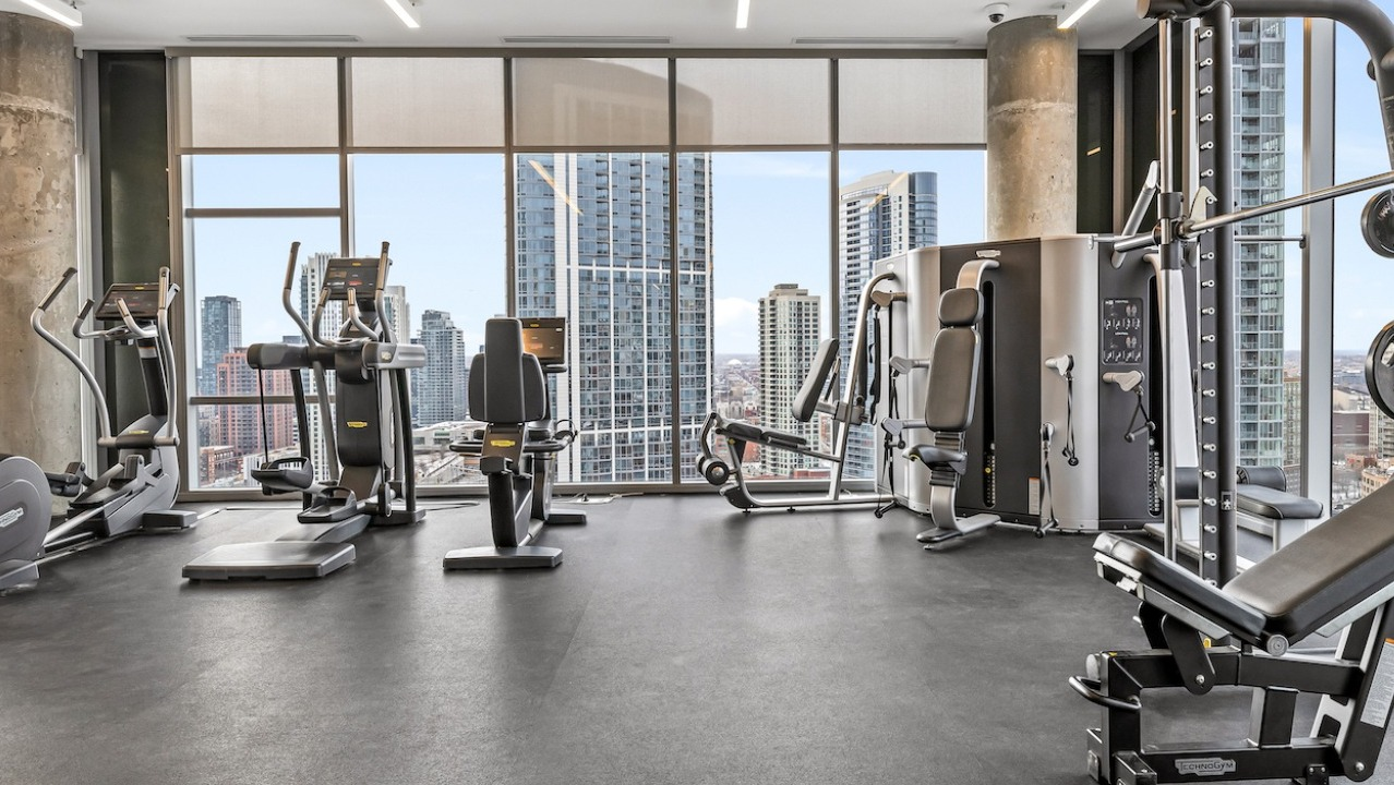 Modern fitness center at 3Eleven Luxury Apartments in Chicago with cardio machines and skyline views through floor-to-ceiling windows