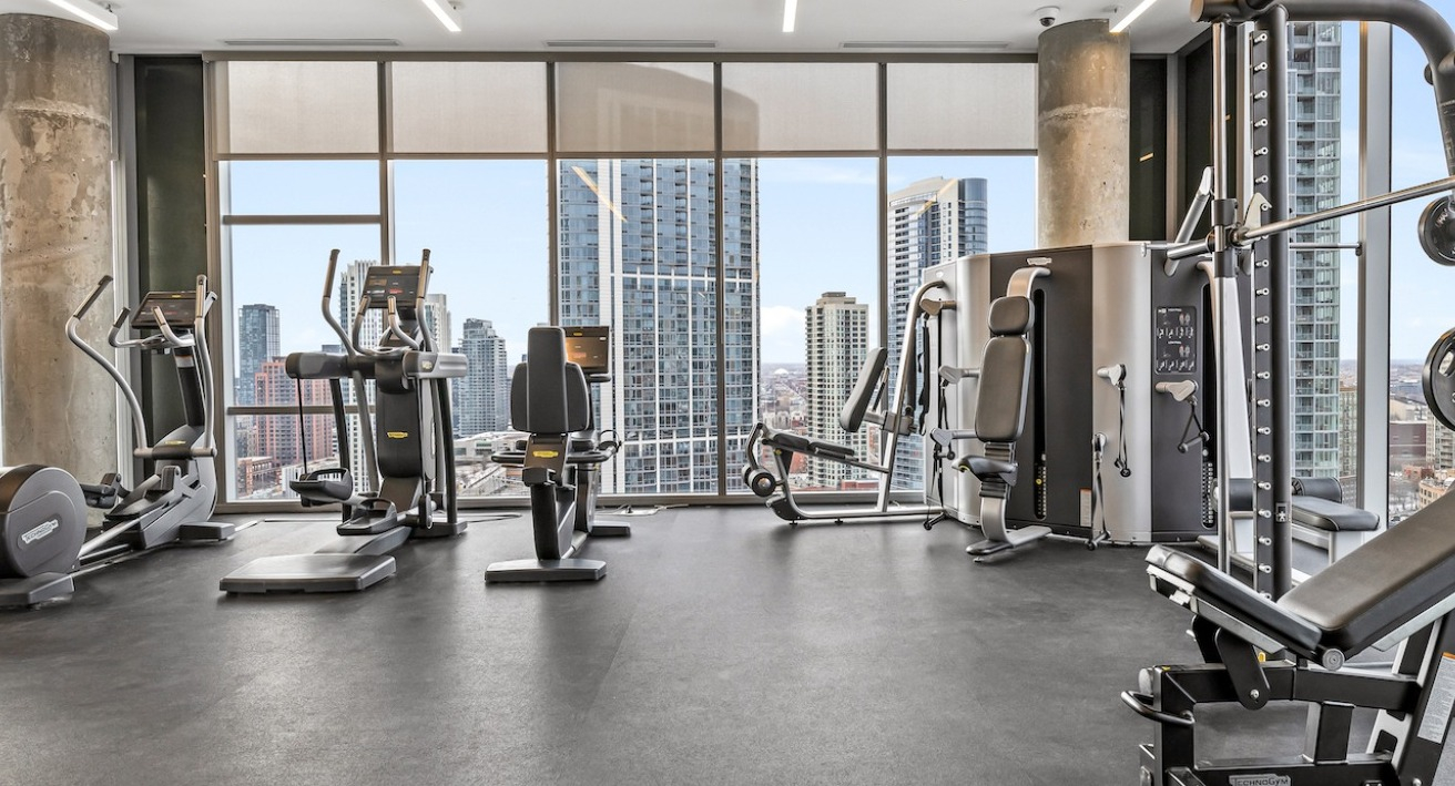 Modern fitness center at 3Eleven Luxury Apartments in Chicago with cardio machines and skyline views through floor-to-ceiling windows