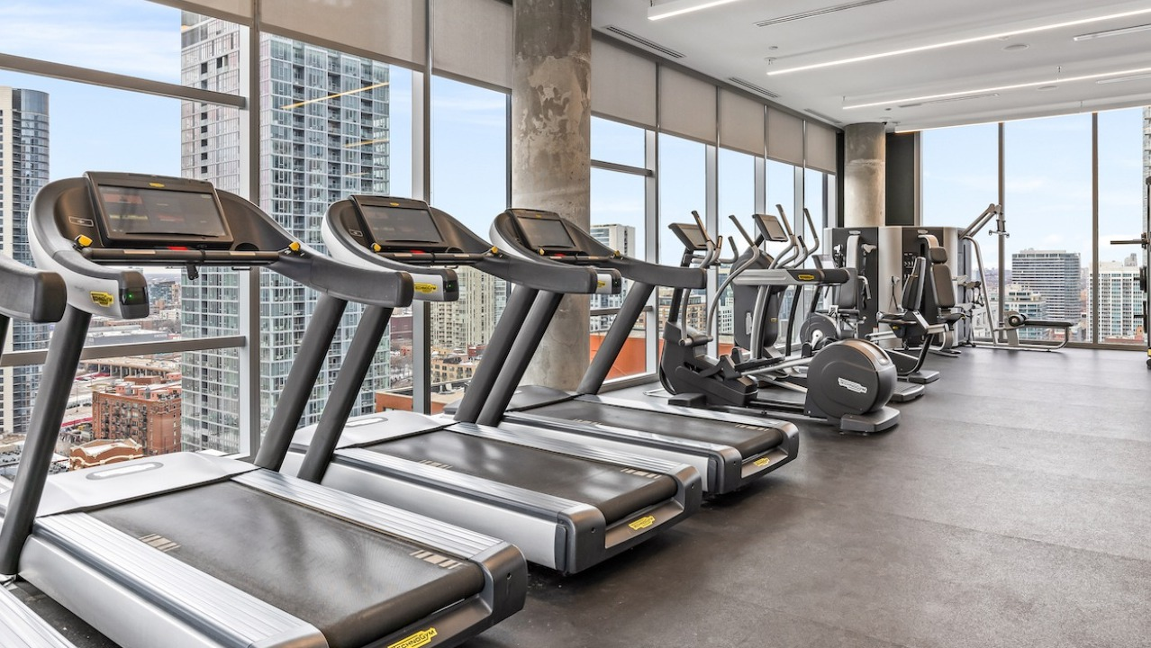 Bright fitness center at 3Eleven Luxury Apartments in Chicago featuring treadmills, ellipticals, and skyline views