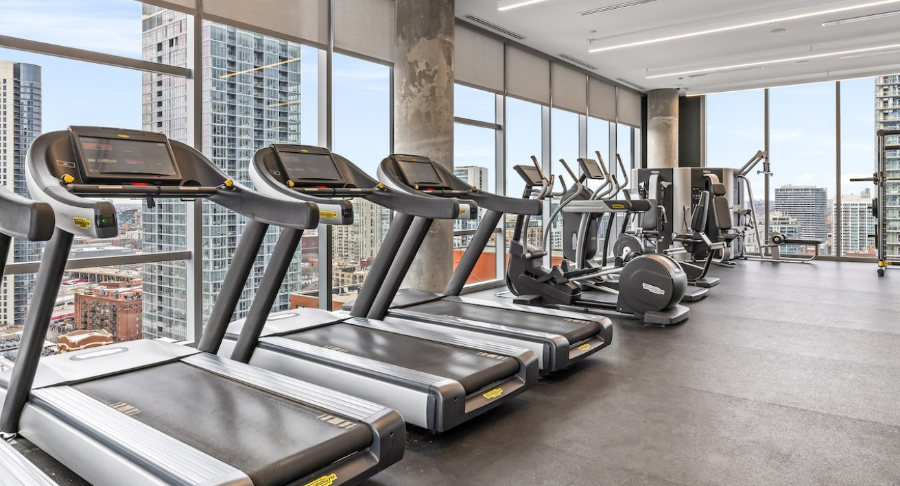 Bright fitness center at 3Eleven Luxury Apartments in Chicago featuring treadmills, ellipticals, and skyline views