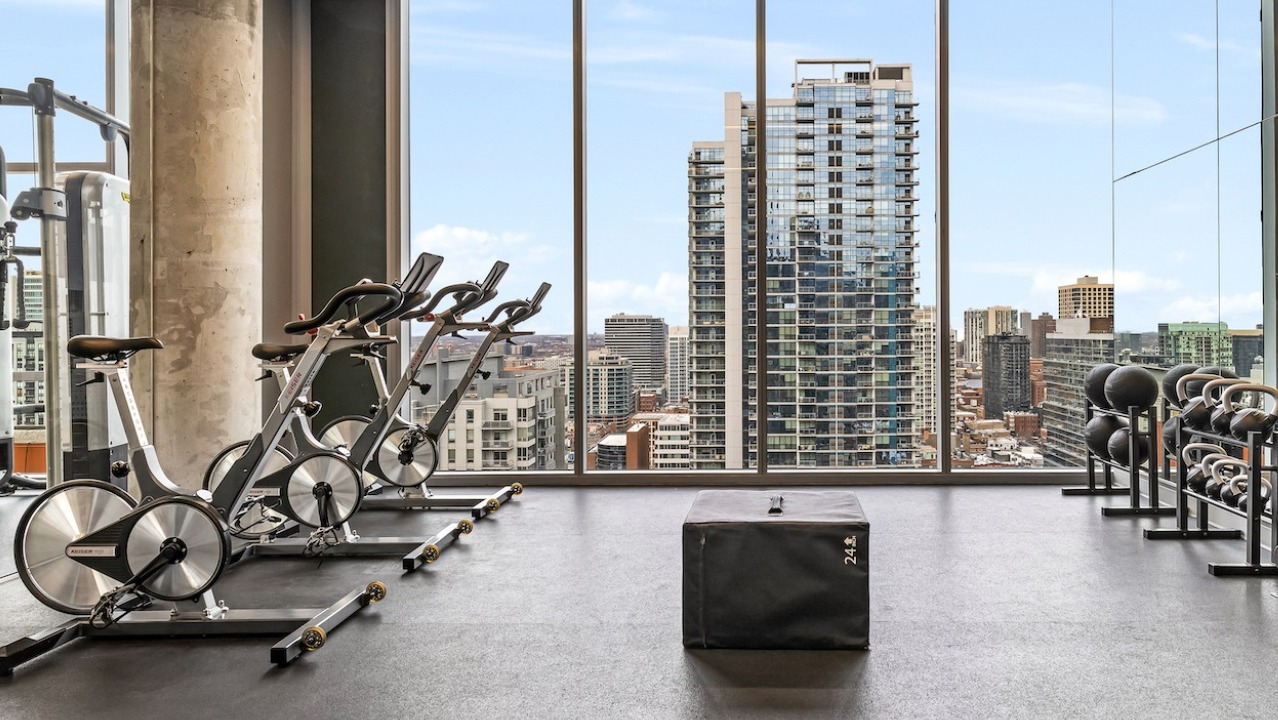 Spacious gym at 3Eleven Luxury Apartments in Chicago with stationary bikes, free weights, kettlebells, and city views