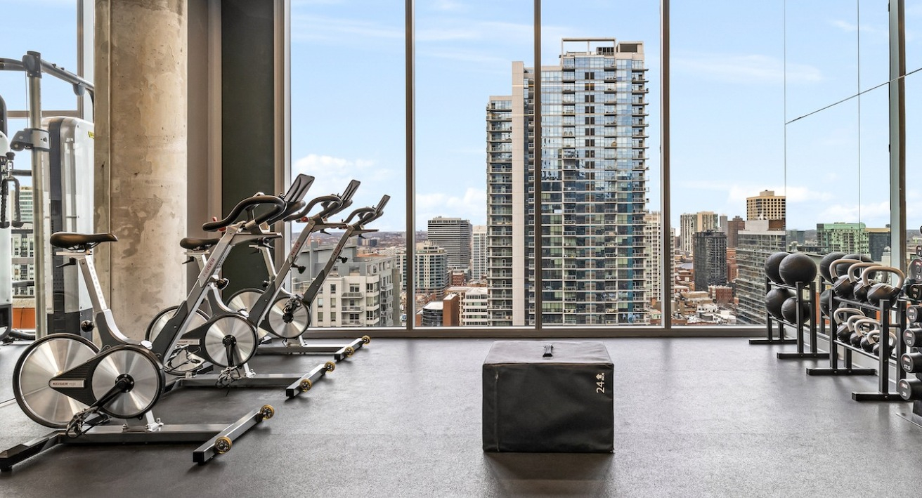 Spacious gym at 3Eleven Luxury Apartments in Chicago with stationary bikes, free weights, kettlebells, and city views
