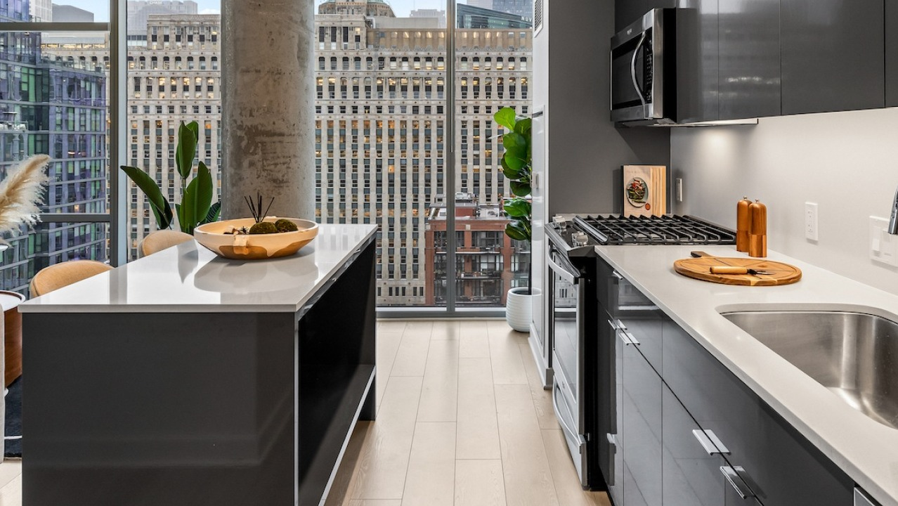 Contemporary kitchen at 3Eleven Luxury Apartments in Chicago with quartz island, gas range, and floor-to-ceiling windows showcasing downtown skyline views