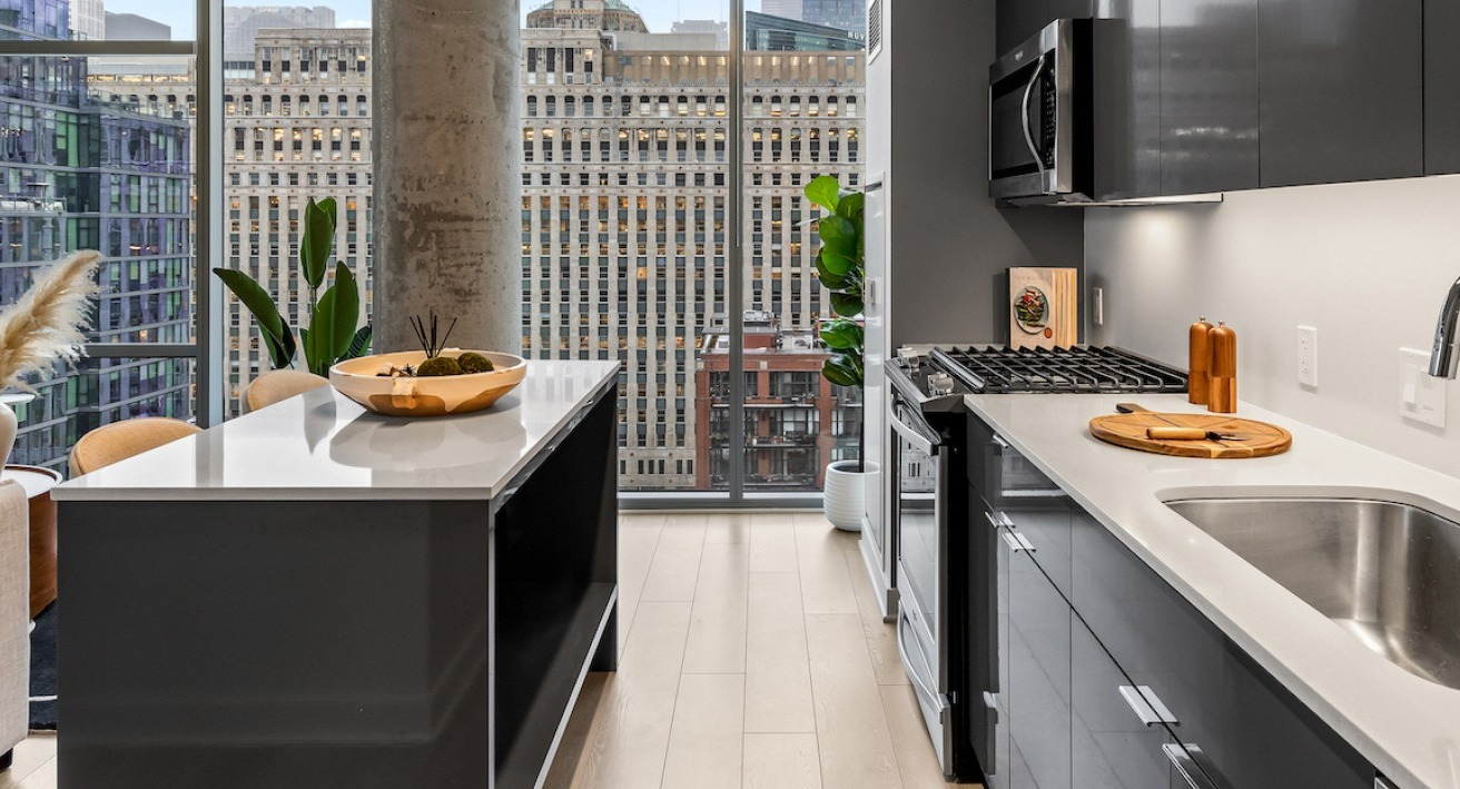 Contemporary kitchen at 3Eleven Luxury Apartments in Chicago with quartz island, gas range, and floor-to-ceiling windows showcasing downtown skyline views