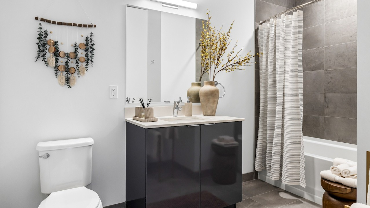 Modern bathroom at 3Eleven Luxury Apartments in Chicago with sleek vanity, large mirror, gray tile tub surround, and neutral decor accents