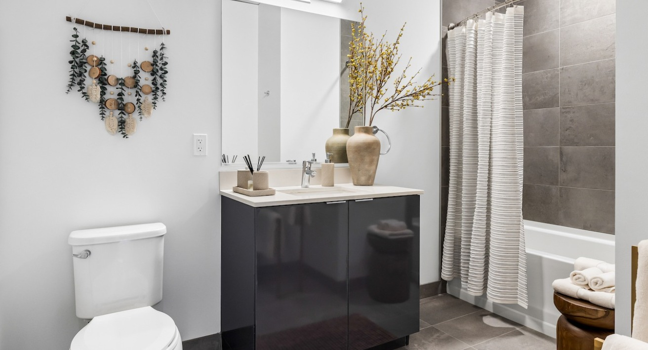 Modern bathroom at 3Eleven Luxury Apartments in Chicago with sleek vanity, large mirror, gray tile tub surround, and neutral decor accents