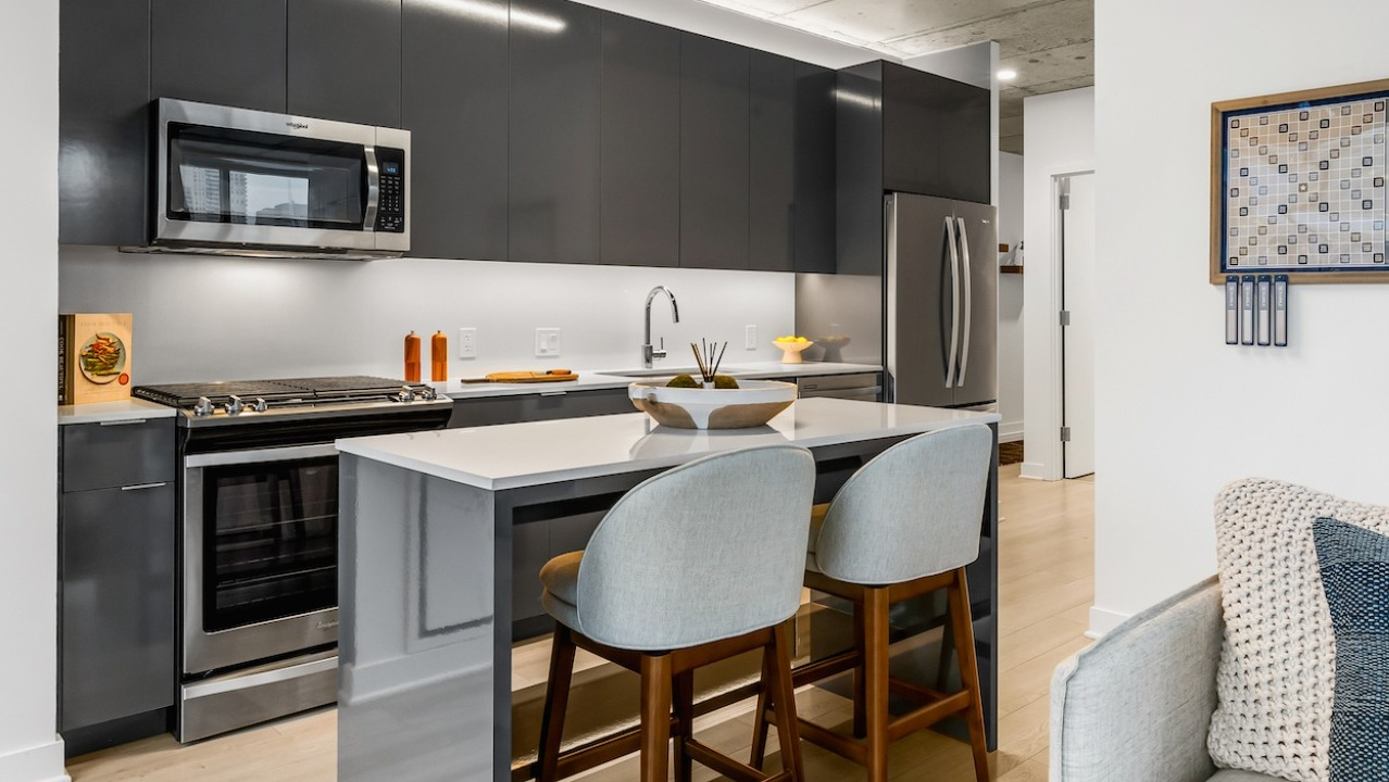 Modern kitchen at 3Eleven Luxury Apartments in Chicago featuring glossy gray cabinets, stainless appliances, and a quartz island with seating for two