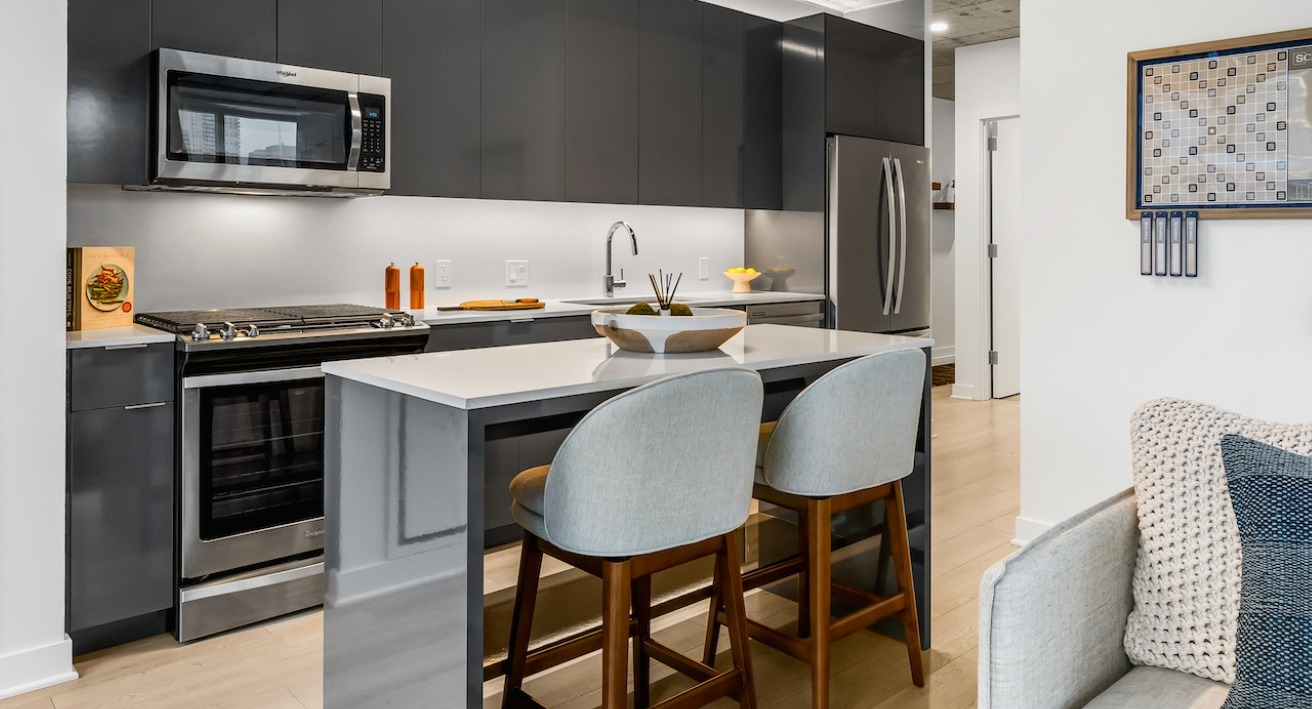 Modern kitchen at 3Eleven Luxury Apartments in Chicago featuring glossy gray cabinets, stainless appliances, and a quartz island with seating for two