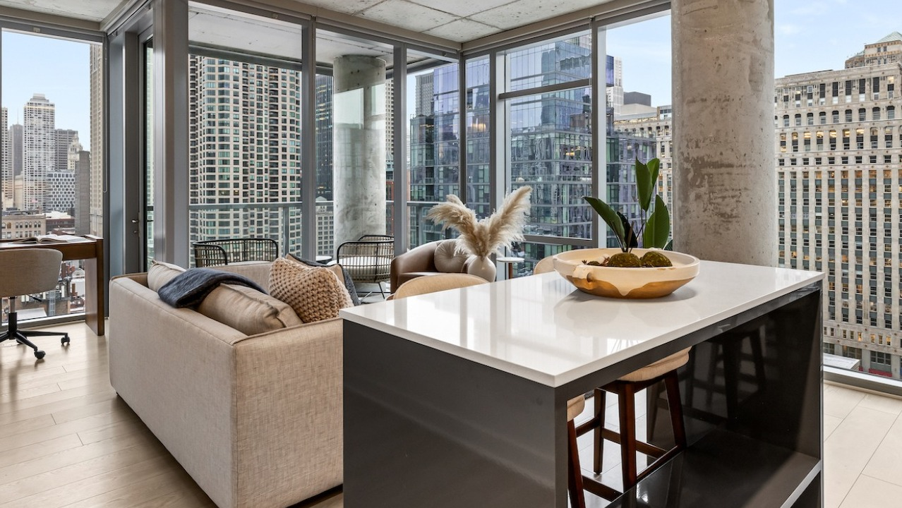 Open-concept living area and kitchen at 3Eleven Luxury Apartments in Chicago with island seating, desk nook, and expansive floor-to-ceiling windows