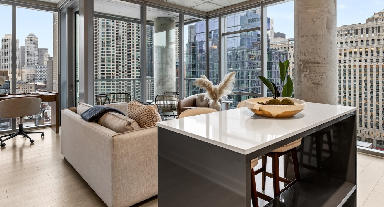 Open-concept living area and kitchen at 3Eleven Luxury Apartments in Chicago with island seating, desk nook, and expansive floor-to-ceiling windows