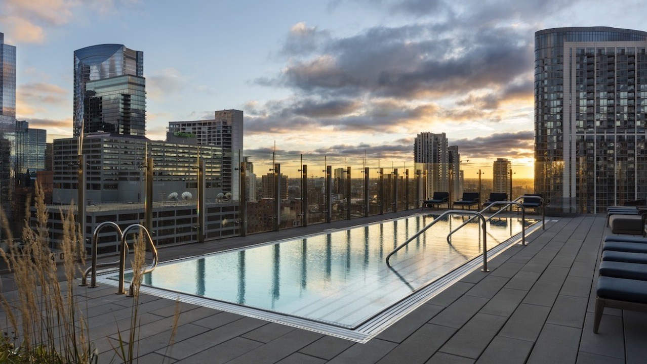 Rooftop swimming pool at 3Eleven Luxury Apartments in Chicago with lounge seating, glass railings, and dramatic downtown skyline views at sunset