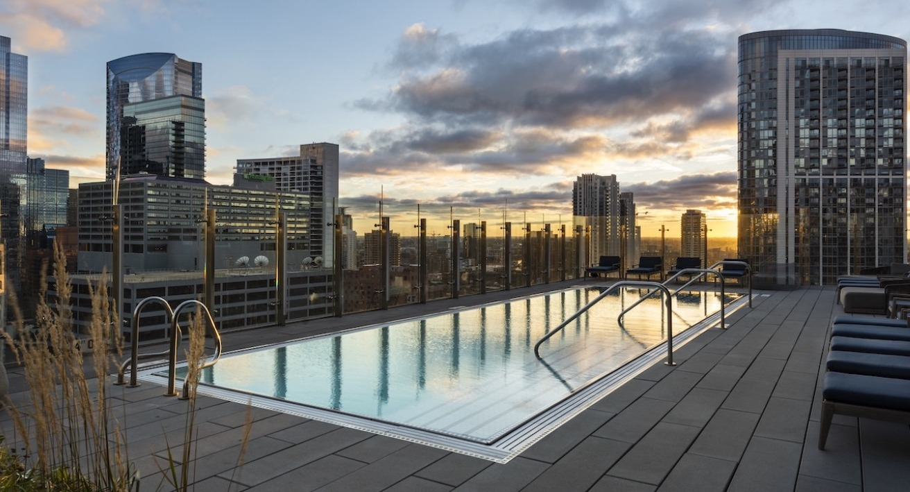 Rooftop swimming pool at 3Eleven Luxury Apartments in Chicago with lounge seating, glass railings, and dramatic downtown skyline views at sunset