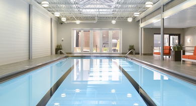 Indoor lap pool with skylight ceiling, bright lighting, and lounge seating at 420 East Ohio apartments in Chicago, designed for year-round swimming