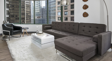 Modern living room with chocolate sectional sofa, arc floor lamp, plush white rug, and panoramic curved windows at 420 East Ohio apartments in Chicago with urban views