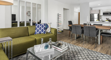 Open-concept living and dining area with green sofa, wood dining table for six, and a modern stainless kitchen at 420 East Ohio apartments in Chicago, perfect for hosting