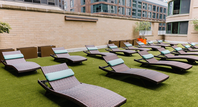 Outdoor sundeck with multiple wicker lounge chairs, green turf, and city views at 420 East Ohio apartments in Chicago, ideal for relaxing and sunbathing