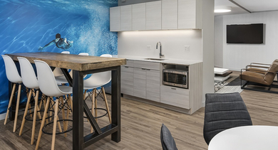 Resident lounge with kitchenette, wood high-top table and stools, and a vibrant blue wall mural at 420 East Ohio apartments in Chicago—great for casual work or gatherings