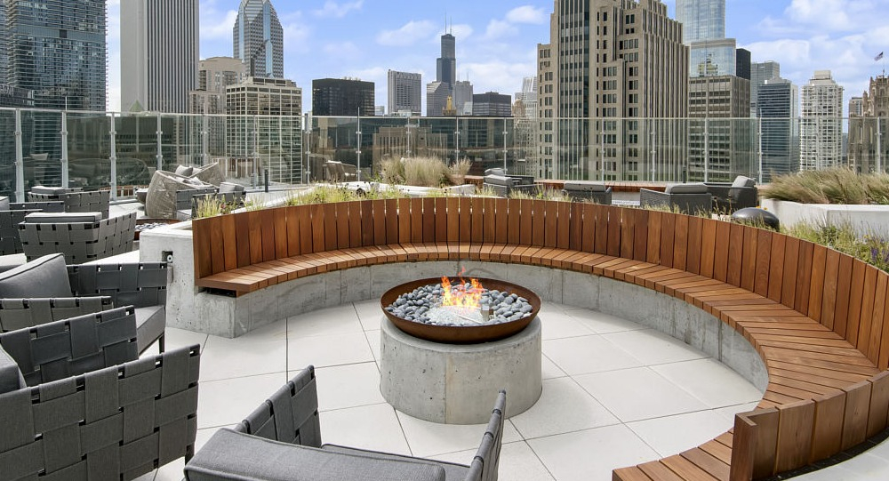 Circular firepit lounge with wood seating and skyline backdrop at 465 North Park apartments in Chicago
