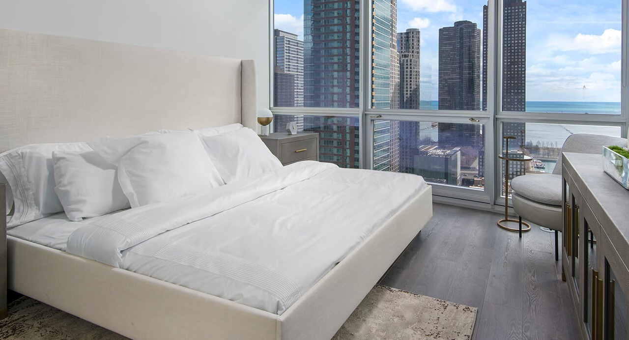 Modern bedroom with large windows, city and lake views, and natural light at 465 North Park apartments in Chicago