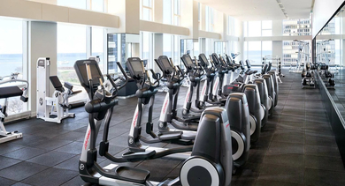 Sunlit fitness center with cardio machines, weight equipment, wall mirrors, and expansive lake views at 500 Lake Shore Drive apartments in Chicago