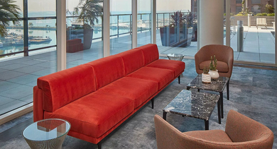 Contemporary indoor lounge with long red sofa, marble coffee tables, and floor-to-ceiling windows overlooking the pool deck at 500 Lake Shore Drive in Chicago