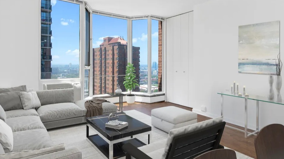 Bright living room with floor-to-ceiling bay windows, gray sectional, accent chair, and city views at 55 West Chestnut apartments in Chicago