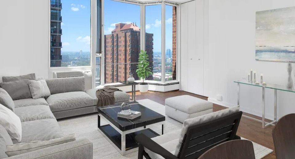 Bright living room with floor-to-ceiling bay windows, gray sectional, accent chair, and city views at 55 West Chestnut apartments in Chicago