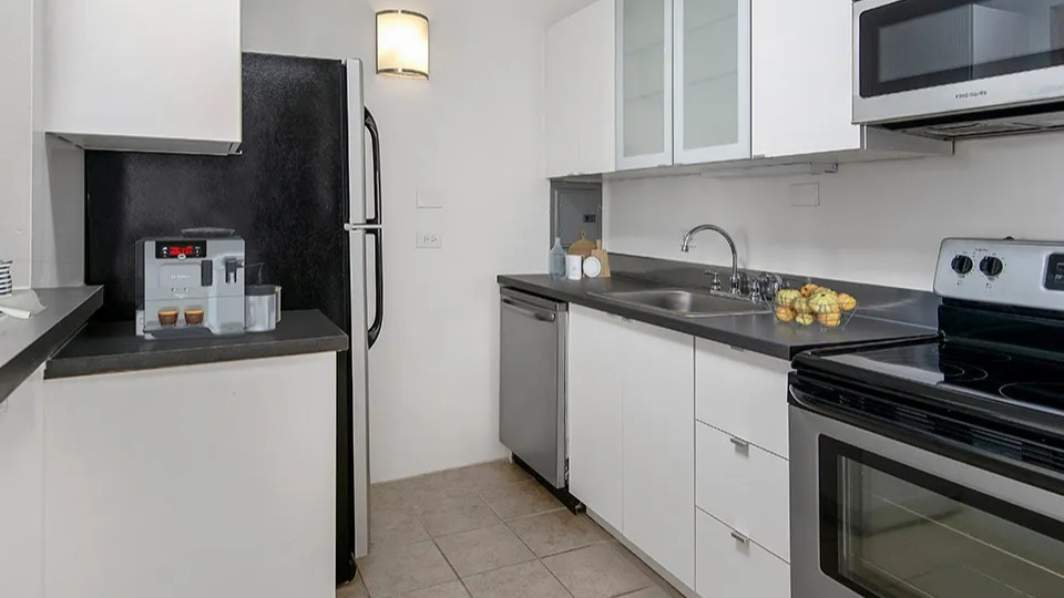 Bright U-shaped kitchen with white cabinetry, black countertops, and stainless appliances at 55 West Chestnut apartments in Chicago, ideal for everyday cooking