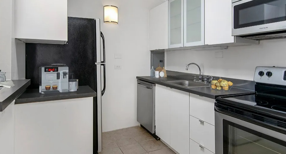 Bright U-shaped kitchen with white cabinetry, black countertops, and stainless appliances at 55 West Chestnut apartments in Chicago, ideal for everyday cooking