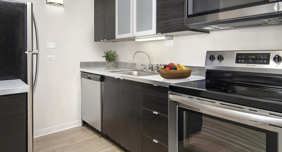 Contemporary L-shaped kitchen with dark wood cabinets, stainless appliances, and light counters creating contrast at 55 West Chestnut apartments in Chicago