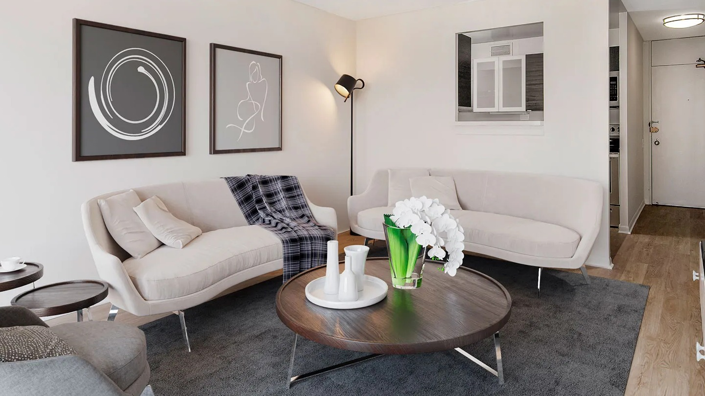 Cozy living room with two cream sofas, round wood coffee table, and soft lighting near a pass-through kitchen at 55 West Chestnut apartments in Chicago