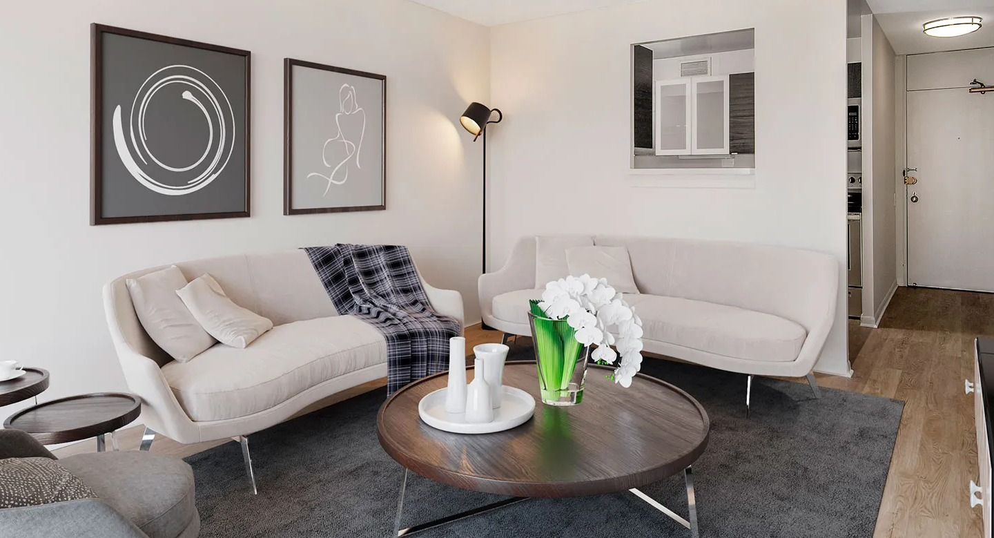 Cozy living room with two cream sofas, round wood coffee table, and soft lighting near a pass-through kitchen at 55 West Chestnut apartments in Chicago