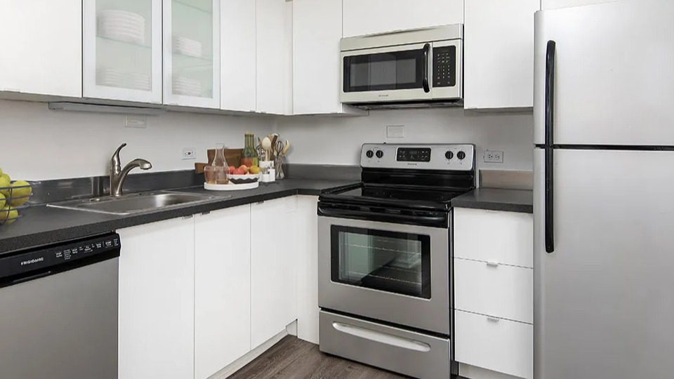 Modern kitchen featuring white cabinets with glass uppers, dark countertops, and stainless appliances at 55 West Chestnut apartments in Chicago, offering a clean look