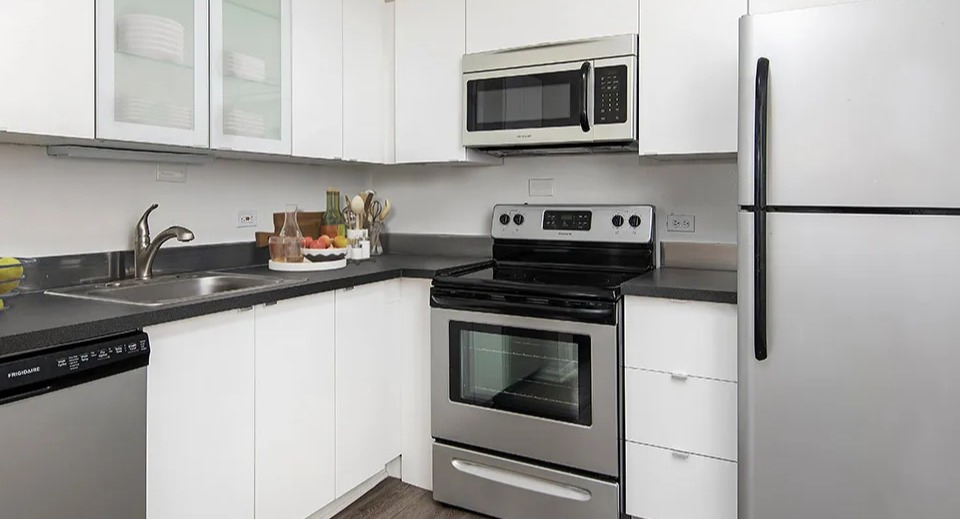 Modern kitchen featuring white cabinets with glass uppers, dark countertops, and stainless appliances at 55 West Chestnut apartments in Chicago, offering a clean look