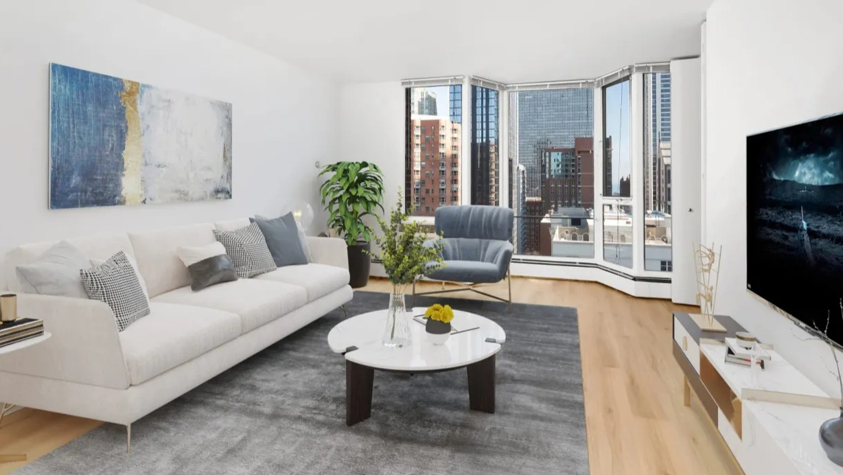 Modern living room with white sofa, gray area rug, round coffee table, TV console, and bay window skyline views at 55 West Chestnut apartments in Chicago