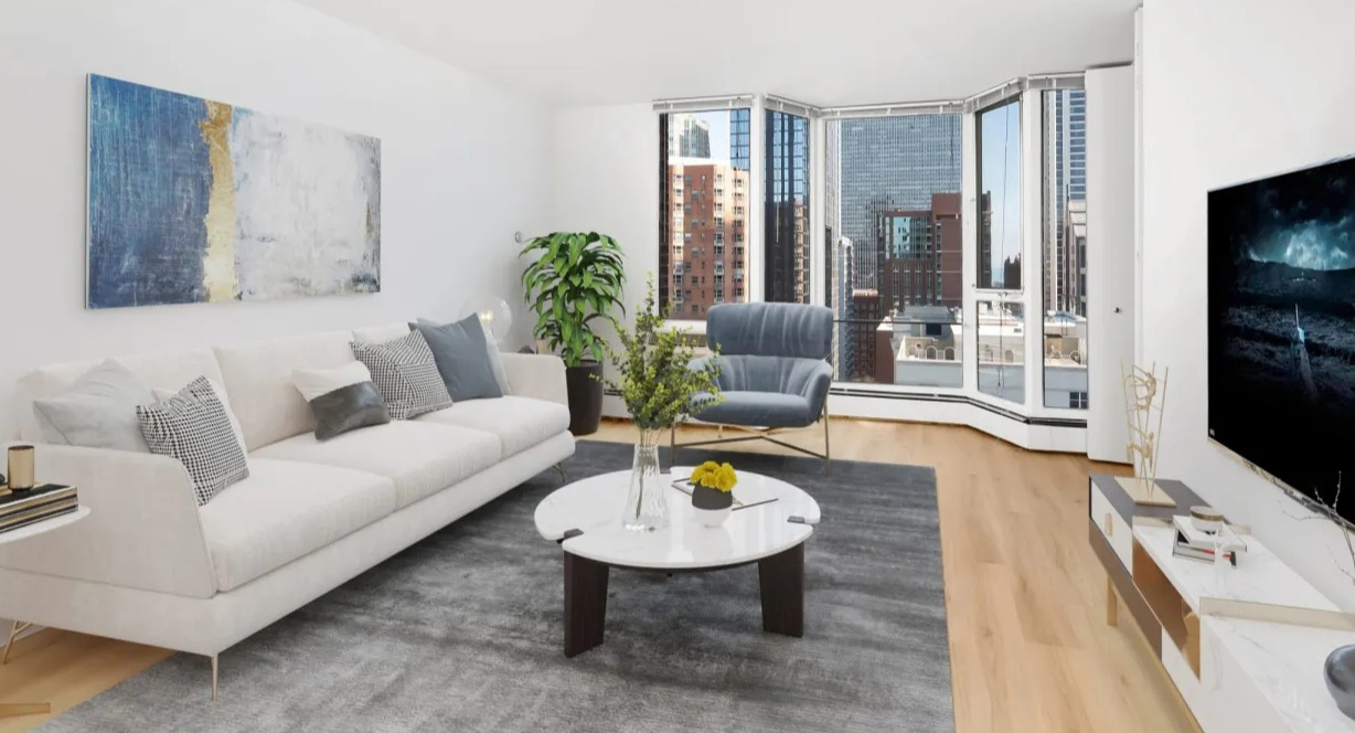 Modern living room with white sofa, gray area rug, round coffee table, TV console, and bay window skyline views at 55 West Chestnut apartments in Chicago